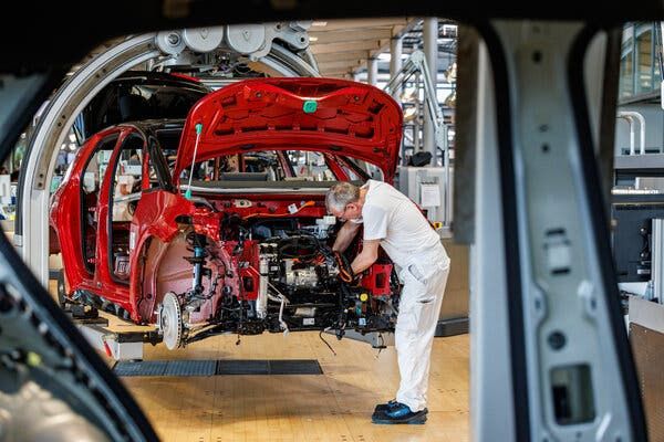 Ein Arbeiter in Weiß montiert Teile an der Karosserie eines roten Autos in einer deutschen Autofabrik.